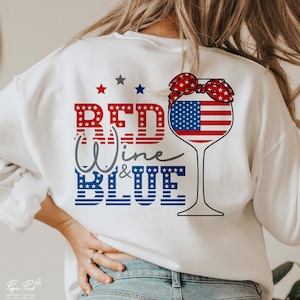 K&ouml;nnte beinhalten: Wei&szlig;es Sweatshirt mit einem rot-wei&szlig;-blauen Design, das ein Weinglas mit einem rot-wei&szlig;-blauen Bandana um den oberen Rand zeigt. Der Text "Red Wine & Blue" ist in rot, wei&szlig; und blau geschrieben.