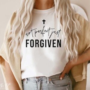 Könnte beinhalten: Ein weißes T-Shirt mit einem schwarzen Kreuz und dem Text "not perfect just FORGIVEN" auf der Vorderseite.