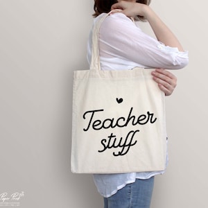 May include: A white canvas tote bag with black text that says "Teacher stuff" and a small black heart above the text.