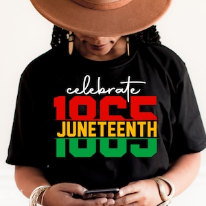 以下が含まれることがあります： 赤、黄、緑の文字で「celebrate 100 Juneteenth 100」と書かれた黒いTシャツです。