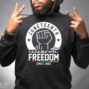 Puede incluir: Sudadera con capucha negra con un diseño gráfico blanco que dice "Juneteenth Celebrate Freedom Since 1865". El gráfico presenta un puño en alto y estrellas.