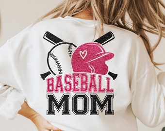 Può includere: Felpa bianca con un design di casco da baseball, palla da baseball e mazze con glitter rosa. Il testo "Baseball Mom" è stampato in nero con un contorno bianco.