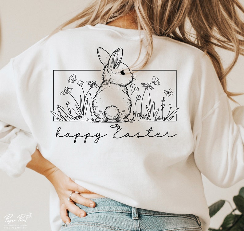 May include: White sweatshirt featuring a black and white illustration of a bunny rabbit in a field of flowers. The text "happy Easter" is printed below the illustration.