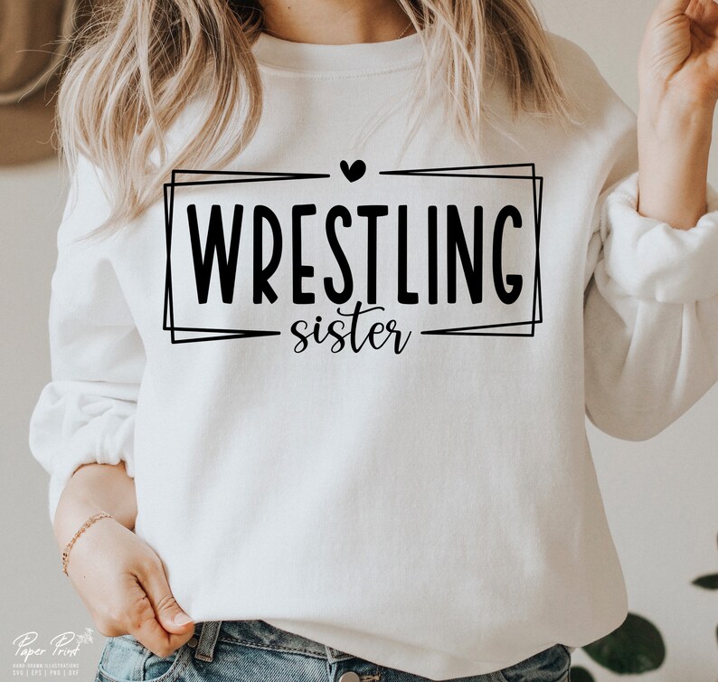 May include: White sweatshirt with black text that reads "Wrestling sister" inside a black frame with a small black heart above the text.