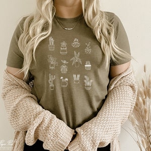 May include: A green t-shirt with a white outline of various potted plants. The shirt has a crew neck and short sleeves.