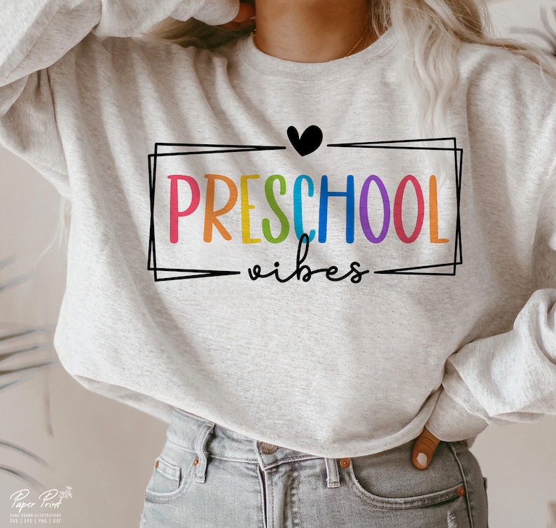 May include: A gray sweatshirt with the text "PRESCHOOL vibes" in rainbow colors inside a black frame. A black heart is above the text.