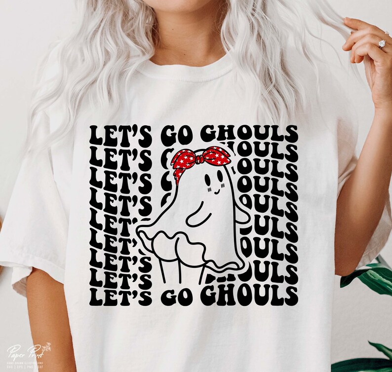 May include: White t-shirt featuring a black and white graphic of a ghost wearing a red bandana with white stars. The text "LET'S GO GHOULS" is repeated in a retro font.