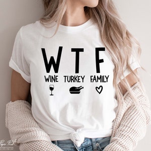 May include: White t-shirt with black text that reads "WTF Wine Turkey Family" with a wine glass, a turkey, and a heart graphic.