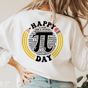 May include: White sweatshirt with a black and yellow graphic design that says "Happy Pi Day". The graphic features a large pi symbol surrounded by numbers.