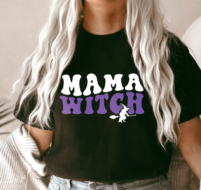 Pu&ograve; includere: Maglietta nera con il testo "Mama Witch" in lettere bianche e viola. Sotto il testo c'&egrave; una silhouette di una strega che cavalca una scopa.