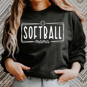 Pu&ograve; includere: Felpa nera con la scritta bianca "SOFTBALL mama" all'interno di un rettangolo bianco. Una grafica di softball &egrave; sopra la parola "SOFTBALL".