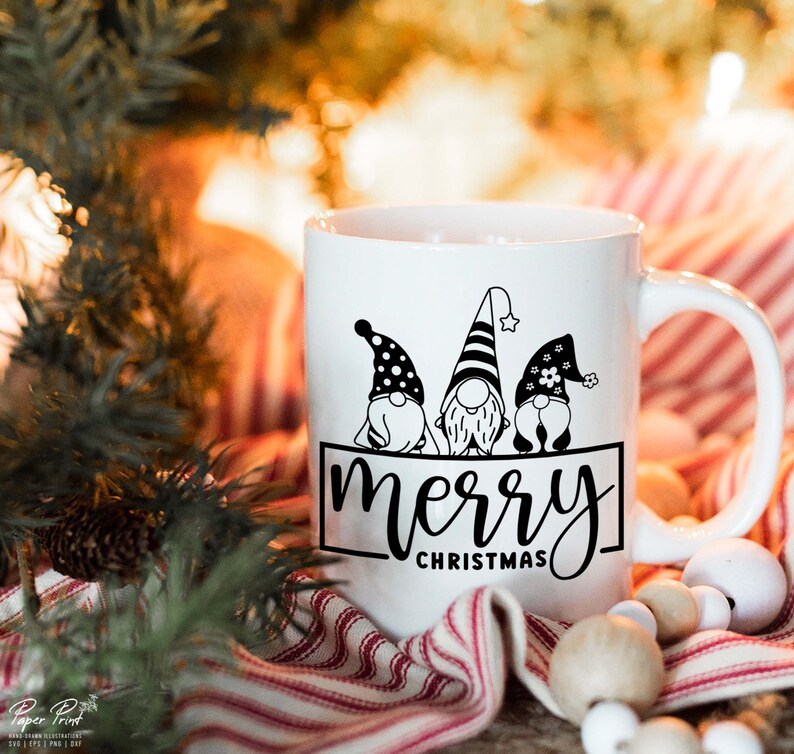K&ouml;nnte beinhalten: Wei&szlig;e Keramiktasse mit einem schwarzen Design aus drei Gnomen mit dem Text "merry christmas".