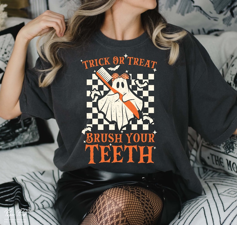 May include: A black t-shirt with a white ghost holding a toothbrush. The text "Trick or Treat Brush Your Teeth" is printed on the shirt in orange.