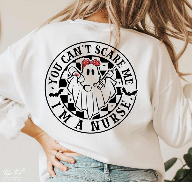 Puede incluir: Sudadera blanca con un gr&aacute;fico en blanco y negro de un fantasma con un pa&ntilde;uelo rojo, sosteniendo un vendaje y una jeringa. El gr&aacute;fico est&aacute; dentro de un c&iacute;rculo con el texto "You Can't Scare Me I'm A Nurse".