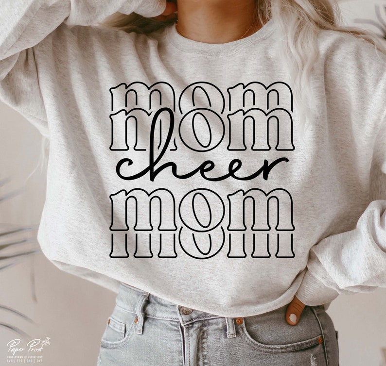 May include: A pale grey sweatshirt featuring the text "mom cheer mom" in black. The word "cheer" is in a cursive font. The sweatshirt is a relaxed fit, ideal for casual wear.