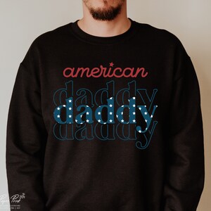 Puede incluir: Sudadera negra con el texto "american daddy" en rojo y azul con estrellas blancas. La palabra "daddy" se repite tres veces, cada repetici&oacute;n es m&aacute;s peque&ntilde;a.
