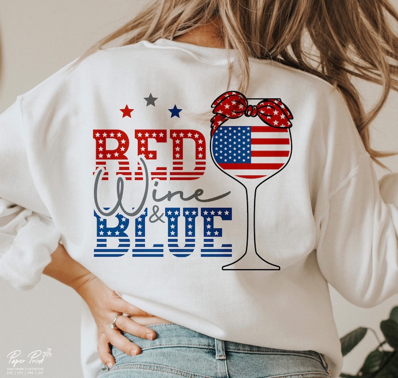 K&ouml;nnte beinhalten: Wei&szlig;es Sweatshirt mit einem rot-wei&szlig;-blauen Design, das ein Weinglas mit einem rot-wei&szlig;-blauen Bandana um den oberen Rand zeigt. Der Text "Red Wine & Blue" ist in rot, wei&szlig; und blau geschrieben.