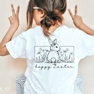 May include: White t-shirt featuring a black and white illustration of a bunny rabbit in a field of flowers. The text "happy Easter" is printed below the illustration.