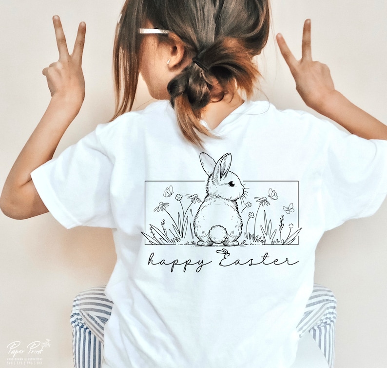 May include: White t-shirt featuring a black and white illustration of a bunny rabbit in a field of flowers. The text "happy Easter" is printed below the illustration.