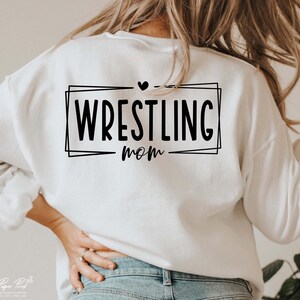 May include: White sweatshirt with black text that reads "Wrestling Mom" inside a black frame with a small heart above the text.