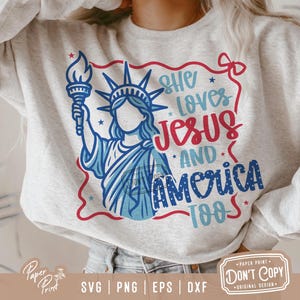 Puede incluir: Una sudadera blanca con un dise&ntilde;o gr&aacute;fico rojo, blanco y azul que presenta a una mujer sosteniendo una antorcha, la Estatua de la Libertad y el texto "She loves Jesus and America too".