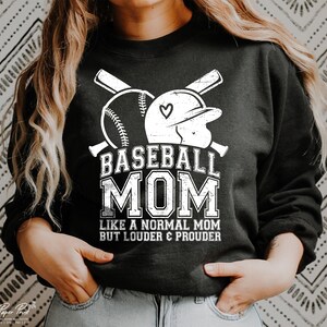 以下が含まれることがあります： 「Baseball Mom Like a Normal Mom But Louder & Prouder」というテキストと、野球ボールと野球帽の白いグラフィックデザインが施された黒いスウェットシャツ。