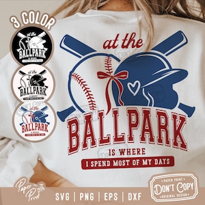 May include: A white t-shirt with a red, white, and blue baseball design. The design includes two baseballs, a baseball cap, and the text "at the ballpark is where I spend most of my days".