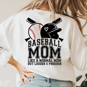 以下が含まれることがあります： 白地に黒と白の野球のグラフィックと「Baseball Mom Like a Normal Mom But Louder & Prouder」というテキストが書かれた白いスウェットシャツ。