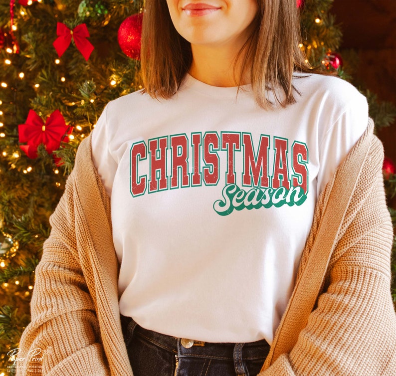 May include: A white t-shirt with a red and green vintage-style graphic that says "Christmas Season".