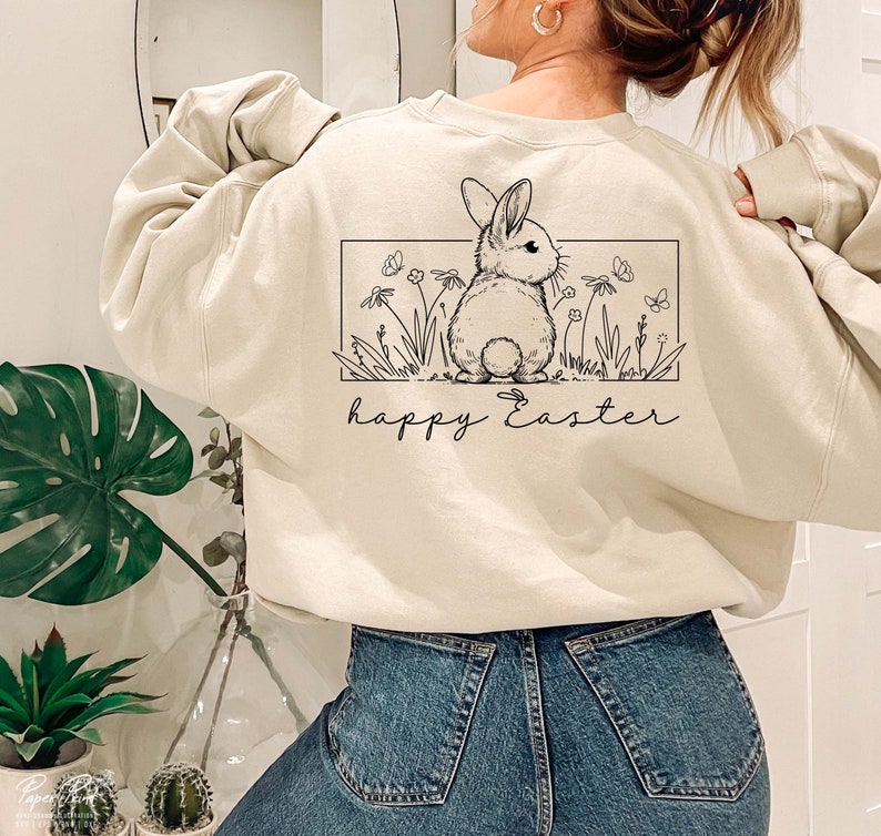 May include: A cream-coloured sweatshirt with a black and white illustration of a bunny rabbit in a field of flowers. The text "happy Easter" is printed below the illustration.