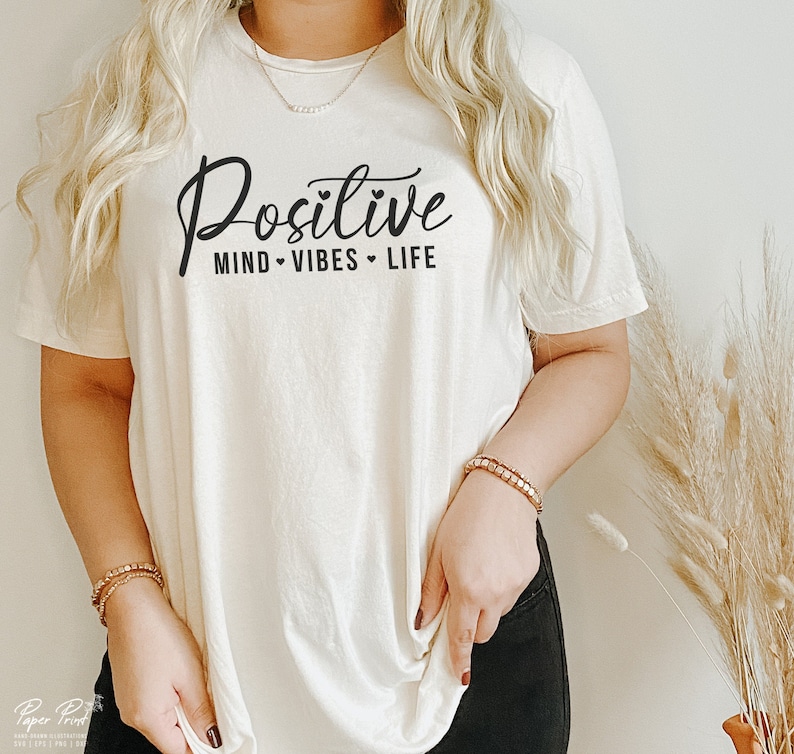 May include: A white t-shirt with the text "Positive Mind Vibes Life" in black script.
