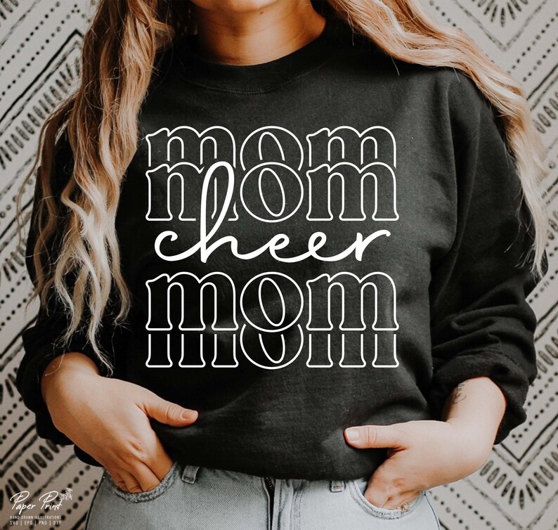 May include: Black sweatshirt with the words "mom cheer mom" in white block letters. The word "cheer" is in a cursive font. The sweatshirt is a crew neck style. The background is a black and white patterned design.