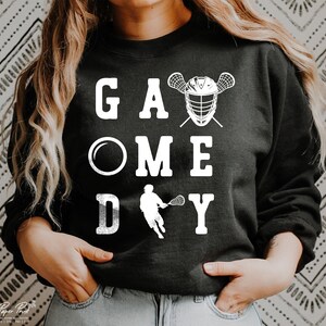 May include: Black sweatshirt with white text that reads "Game Day" with a lacrosse stick and helmet graphic.
