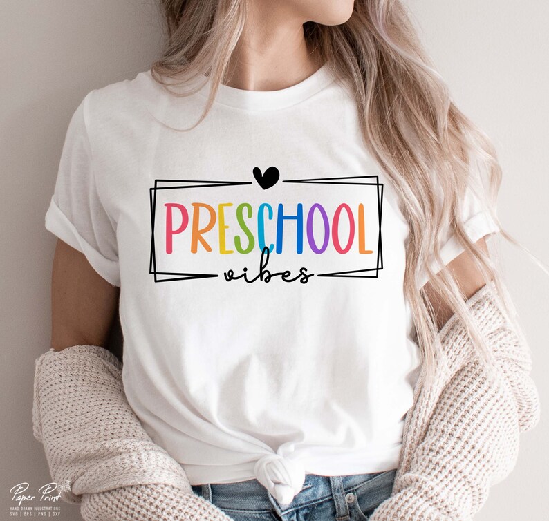 May include: White t-shirt with a rainbow colored text that says "PRESCHOOL vibes" inside a black frame with a black heart above the text.