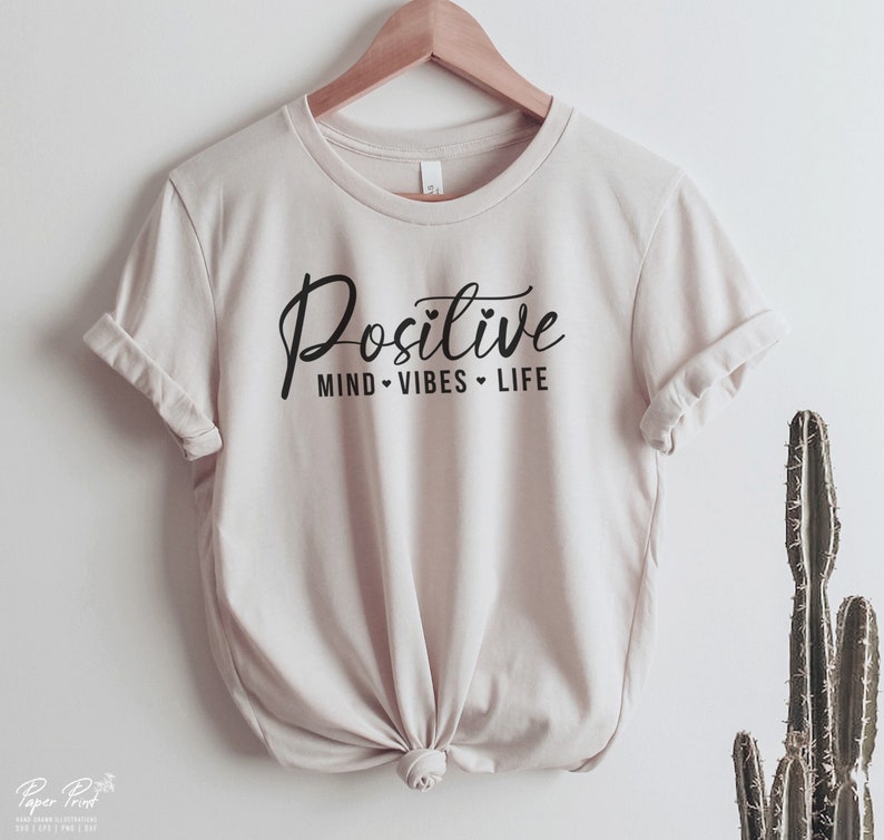 May include: A beige t-shirt with the text "Positive Mind - Vibes - Life" printed in black.