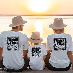 Puede incluir: Una familia de tres personas con camisetas blancas con un dise&ntilde;o de sello negro que dice "Beach Vibes" y el texto "Great Memories, Great Laughs, Great Times, Great Family". La familia est&aacute; sentada en una playa al atardecer.