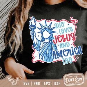 Puede incluir: Una camiseta negra con un dise&ntilde;o gr&aacute;fico rojo, blanco y azul que presenta la Estatua de la Libertad y el texto "She Loves Jesus And America Too".