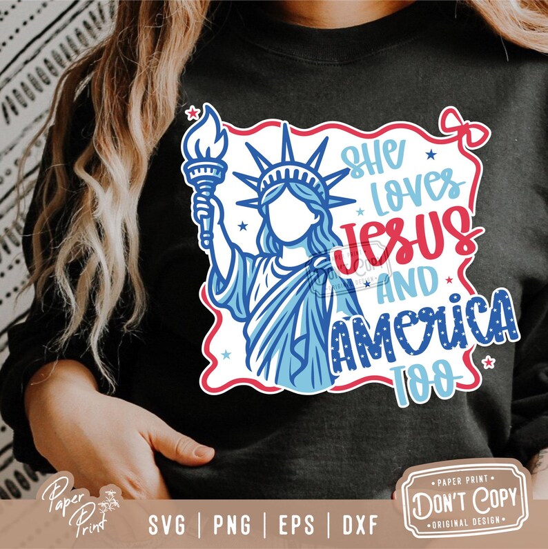 Puede incluir: Una camiseta negra con un dise&ntilde;o gr&aacute;fico rojo, blanco y azul que presenta la Estatua de la Libertad y el texto "She Loves Jesus And America Too".