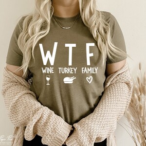 May include: A green t-shirt with the text "WTF" and the words "Wine, Turkey, Family" underneath. The words are in white and there are icons of a wine glass, a turkey, and a heart.