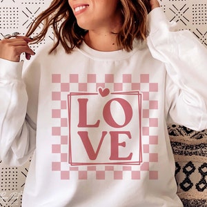 May include: White sweatshirt with a pink and white checkered pattern and the word "LOVE" in pink letters.