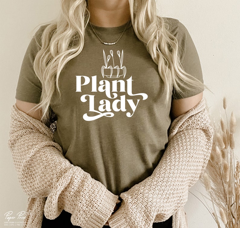 May include: A woman wearing a green t-shirt with the text "Plant Lady" in white lettering. The shirt features a simple line drawing of a potted plant with leaves.