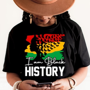May include: Black t-shirt with a graphic of a woman's silhouette with butterflies in her hair. The graphic is in red, yellow, and green colors. The text "I am Black HISTORY" is printed in white below the graphic.