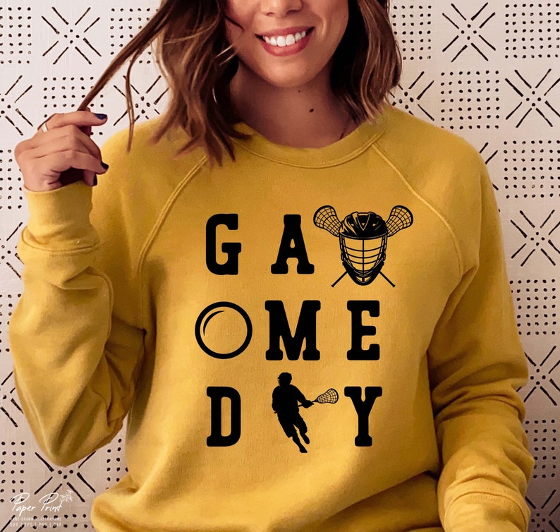 May include: A yellow sweatshirt with the text "Game Day" printed in black. The text is stylized with a lacrosse stick and ball graphic.