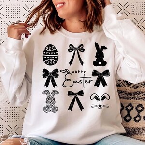 May include: White sweatshirt with a black graphic design featuring a bunny, bows, an egg, and the text "Happy Easter".