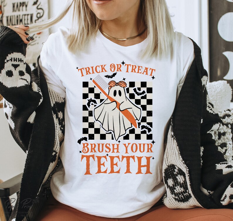 May include: White t-shirt with a graphic of a ghost holding a toothbrush. The text "Trick or Treat" is above the ghost and "Brush Your Teeth" is below the ghost.