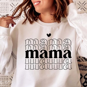 May include: White sweatshirt with a black graphic design that says "mama" in a stacked, layered font. A small black heart is above the word.
