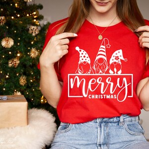 K&ouml;nnte beinhalten: Rotes T-Shirt mit einer wei&szlig;en Grafik von drei Gnomen, die Weihnachtsm&uuml;tzen tragen, und dem Text "merry christmas".