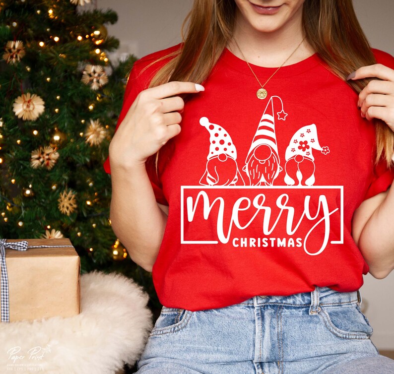K&ouml;nnte beinhalten: Rotes T-Shirt mit einer wei&szlig;en Grafik von drei Gnomen, die Weihnachtsm&uuml;tzen tragen, und dem Text "merry christmas".