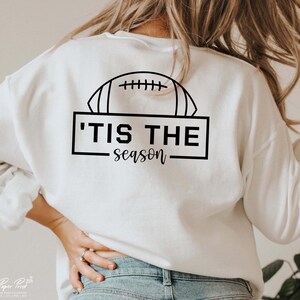 May include: White sweatshirt with a black graphic of a football and the text 'Tis the season.