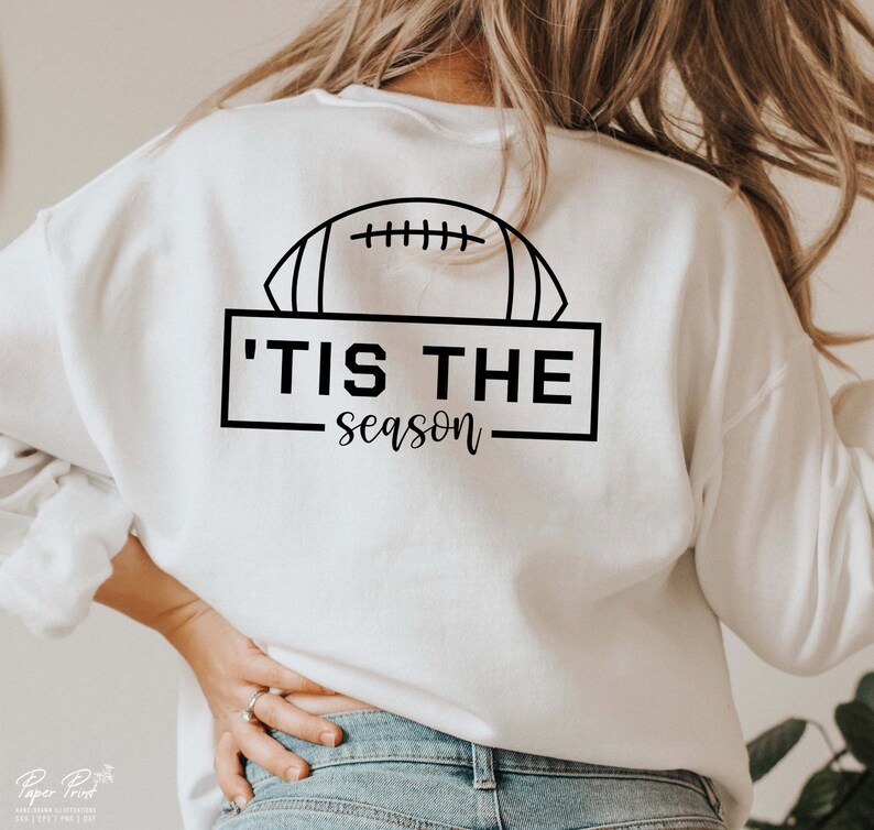 May include: White sweatshirt with a black graphic of a football and the text 'Tis the season.